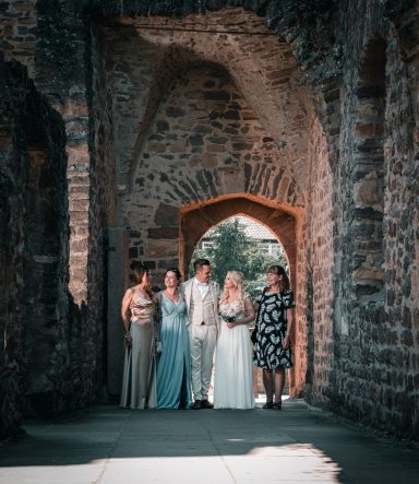 Gruppe von sechs Personen in formeller Kleidung, stehend in einem historischen Gang.