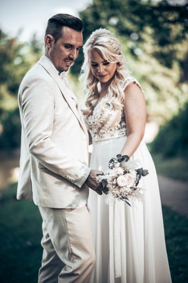 Brautpaar in eleganter Hochzeitskleidung, umarmt und schaut sich liebevoll an.